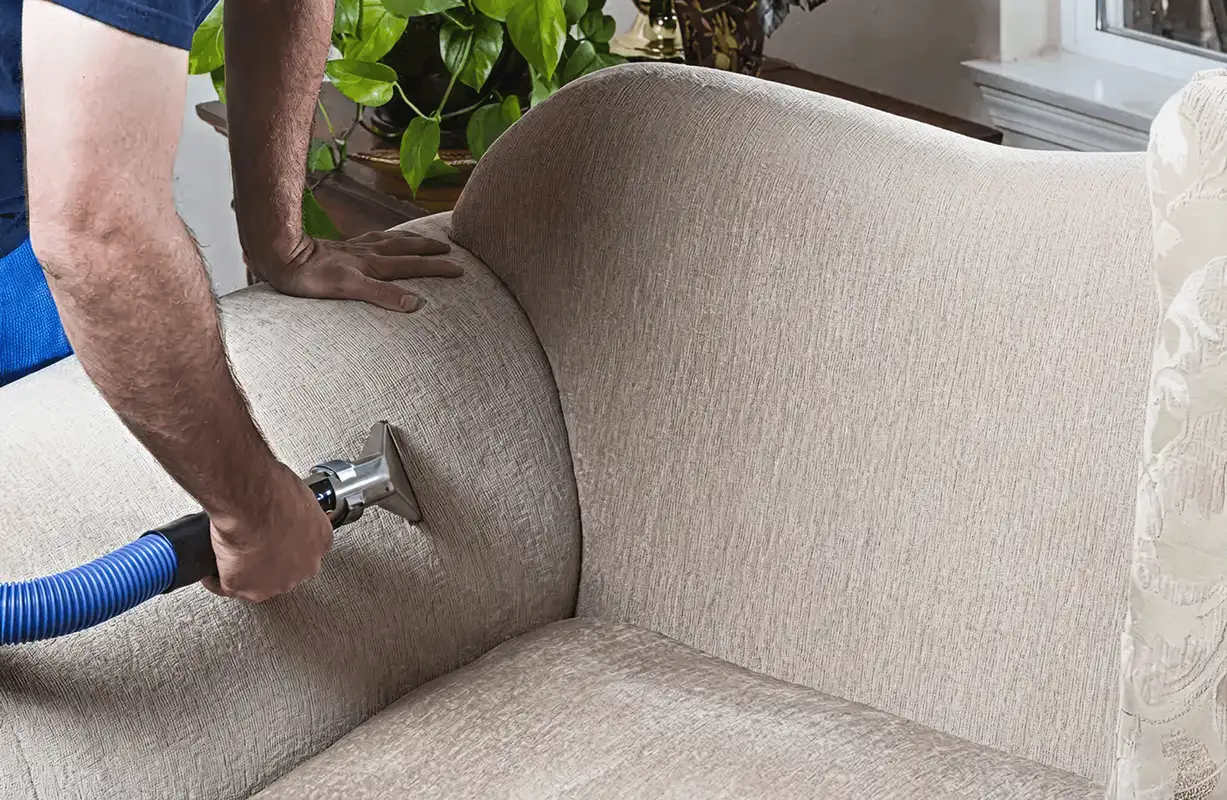 Professional upholstery cleaner deep-cleaning a fabric sofa with a handheld extraction tool and hose, Myrtle Beach, SC.